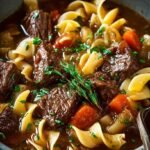 A steaming bowl of beef and noodles stew with carrots and celery in a rich brown gravy.