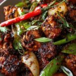 A skillet of savory black pepper chicken with sliced onions and celery in a dark glossy sauce.