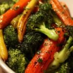A baking sheet filled with golden roasted broccoli florets and caramelized carrot coins seasoned with garlic and thyme.