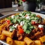 A large skillet filled with cheesy enchilada pasta topped with melted cheese and fresh cilantro.