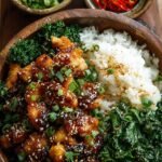 A bowl of crispy sesame chicken over jasmine rice with steamed broccoli and green onion garnish