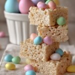 Square cut Easter rice krispie treats with pastel sprinkles and mini chocolate eggs on a white plate.