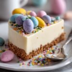 A creamy vanilla cheesecake in a springform pan topped with whipped cream dollops and pastel mini chocolate eggs.