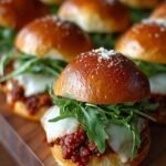 A tray of golden brown pull-apart pizza sliders with melted cheese and pepperoni on Hawaiian rolls.