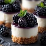 Mini cheesecakes with a purple blackberry swirl and graham cracker crust on a white platter.