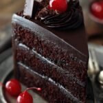 A stunning two-layer dark chocolate cake with glossy chocolate ganache on a serving plate.