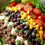 A vibrant high protein taco salad bowl with ground beef, black beans, avocado, and creamy lime dressing.