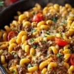 A large black skillet filled with creamy cheeseburger pasta and melted cheddar cheese.