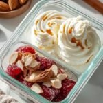 A divided meal prep container filled with smooth whipped cottage cheese, cucumbers, tomatoes, almonds, and crackers.