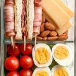 A meal prep container filled with turkey, ham, bacon, lettuce wraps, avocado, and a hard-boiled egg.