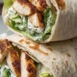 Two sliced high protein chicken caesar wraps filled with grilled chicken, romaine lettuce, and creamy dressing on a white plate.