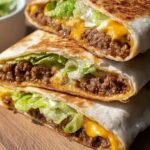 A golden brown, toasted hexagonal crunchwrap cut in half showing layers of beef, cheese, and lettuce.