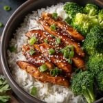 A bowl of shredded teriyaki chicken over jasmine rice with steamed broccoli and sesame seeds