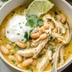 A white bowl filled with creamy white chicken chili topped with cilantro and avocado