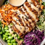 A colorful sesame ginger chicken salad with grilled chicken, purple cabbage, and julienned carrots in a large bowl.