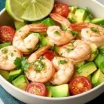 A fresh bowl of shrimp avocado salad with cucumber and red onion served over baby spinach.