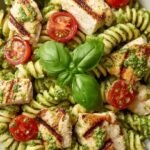 A bowl of high protein chicken pesto pasta salad with cherry tomatoes and spinach
