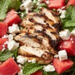 A fresh bowl of cubed watermelon, grilled chicken, and feta cheese with mint leaves.