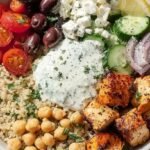 A vibrant Mediterranean power bowl with grilled chicken, quinoa, chickpeas, and fresh vegetables drizzled with tahini dressing.