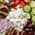 A fresh Greek Gyro Salad with spiced lamb strips, feta cheese, and creamy tzatziki dressing in a white bowl.