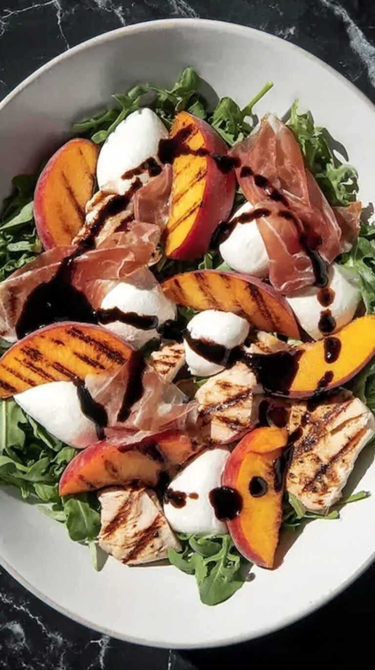 A vibrant salad with grilled peaches, sliced chicken, prosciutto ribbons, and mozzarella pearls on baby arugula.