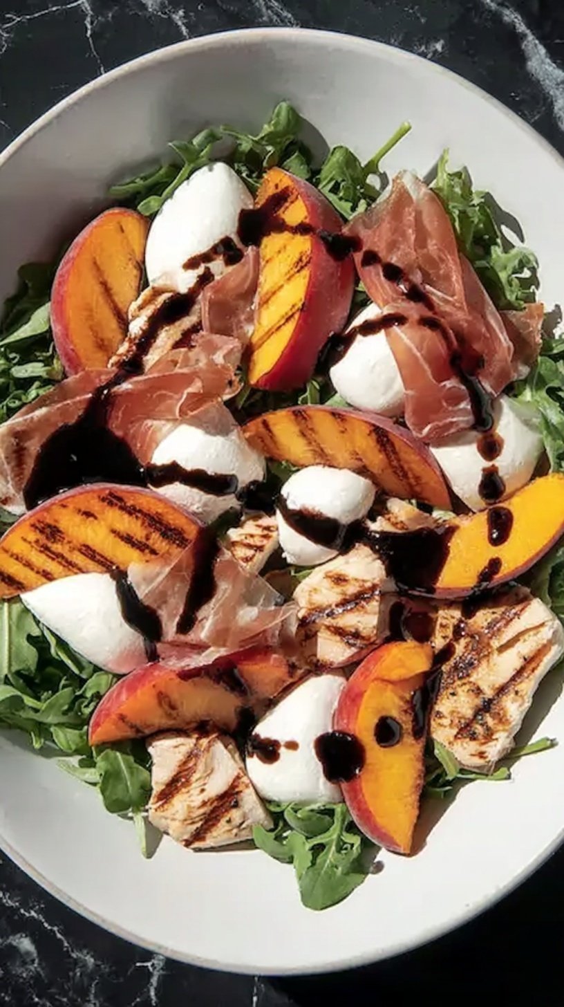 A vibrant salad with grilled peaches, sliced chicken, prosciutto ribbons, and mozzarella pearls on baby arugula.