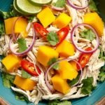 A vibrant bowl of shredded chicken salad with julienned mango, red peppers, and cilantro in a lime dressing.