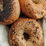 Four golden brown whole wheat bagels resting on a wire cooling rack