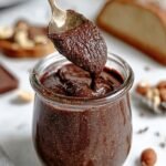 A jar of creamy homemade sugar-free hazelnut chocolate spread with whole hazelnuts nearby