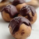 Chocolate coated peanut butter protein truffles topped with crushed peanuts on a tray.