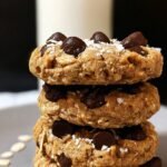A stack of thick and chewy oatmeal cookies made with powdered peanut butter on a parchment-lined baking sheet.