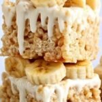 A stack of yellow-tinted marshmallow cereal bars with crushed vanilla wafers and dried banana chips on a white platter.