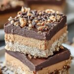 A stack of square chocolate-topped peanut butter sandwich bars on a white plate.