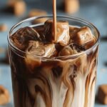 A tall glass of cold brew coffee topped with a thick layer of peanut butter cold foam and ice cubes.