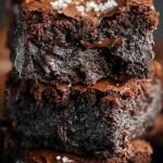 A stack of thick, fudgy homemade brownies with a shiny crackly top on a wire cooling rack.