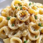 A close up of garlic butter pasta with fresh parsley and grated parmesan cheese in a white bowl.