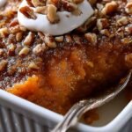 A baking dish filled with Sweet Potato Crunch Dessert topped with golden brown pecans.