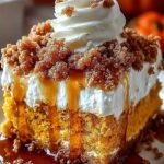 A slice of pumpkin poke cake topped with whipped cream, caramel drizzle, and toffee bits on a white plate.