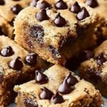 A stack of thick, chewy chocolate chip bars with melted chocolate chips on a cooling rack.