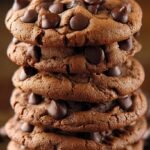 A stack of thick, soft chocolate chip cookies with melty chocolate chips on a cooling rack.