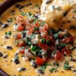 A cast iron skillet filled with melted Cowboy Queso Dip topped with cilantro and surrounded by tortilla chips.