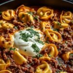 A skillet filled with cheesy beef enchilada tortellini topped with melted cheese and fresh cilantro.