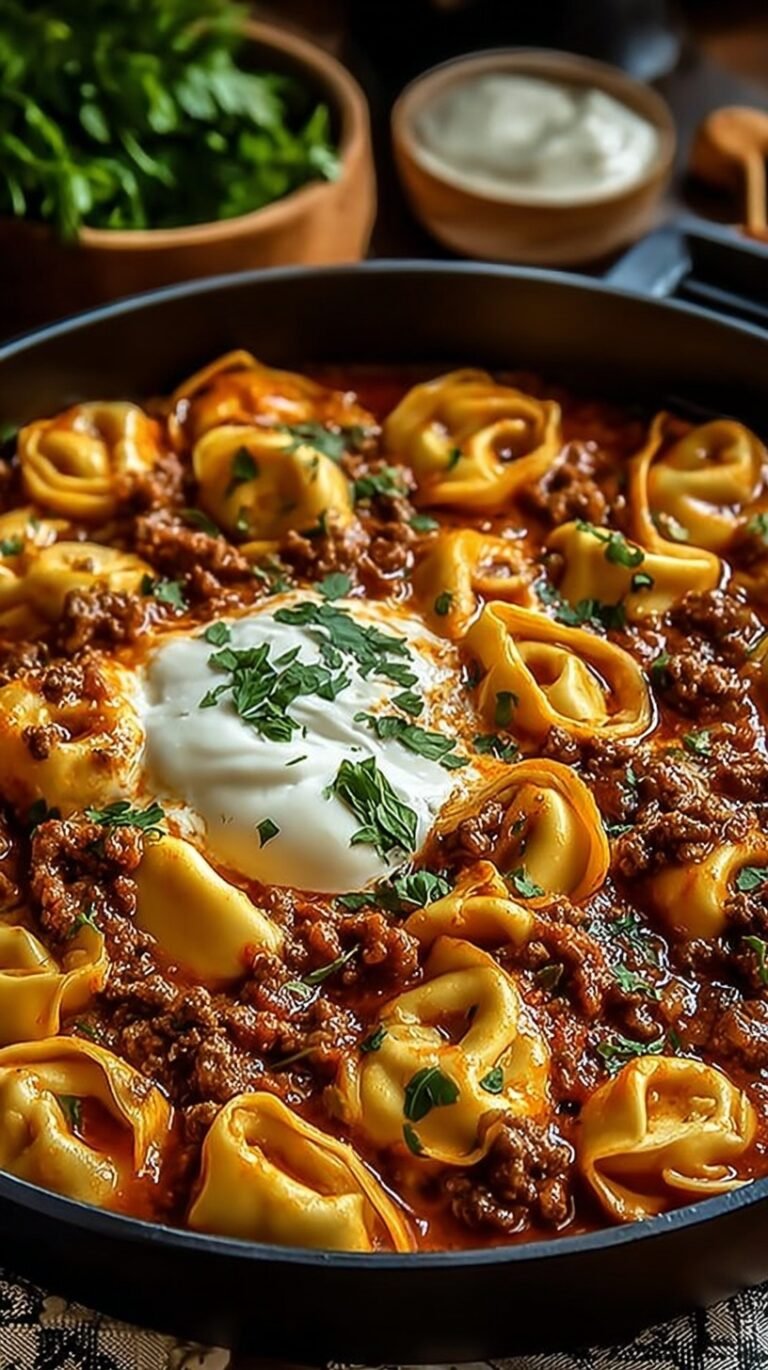 A skillet filled with cheesy beef enchilada tortellini topped with melted cheese and fresh cilantro.