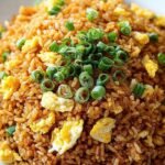 A steaming bowl of egg fried rice with green onions and colorful peas and carrots