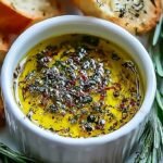 A shallow bowl of golden olive oil with balsamic vinegar and dried herbs for bread dipping.