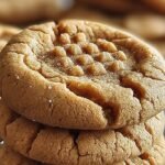 A stack of thick, golden brown peanut butter cookies with traditional fork criss-cross marks on a cooling rack.