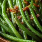 A baking dish filled with glazed green beans topped with crumbled bacon bits