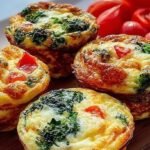 A tray of golden-baked egg white muffins filled with red peppers and green spinach.