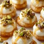 Crispy baguette slices topped with whipped ricotta, chopped pistachios, and a drizzle of honey on a wooden serving board.