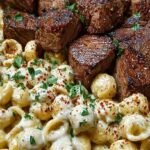 Seared garlic butter steak bites served over a bowl of creamy white cheddar shell pasta with chipotle sauce.